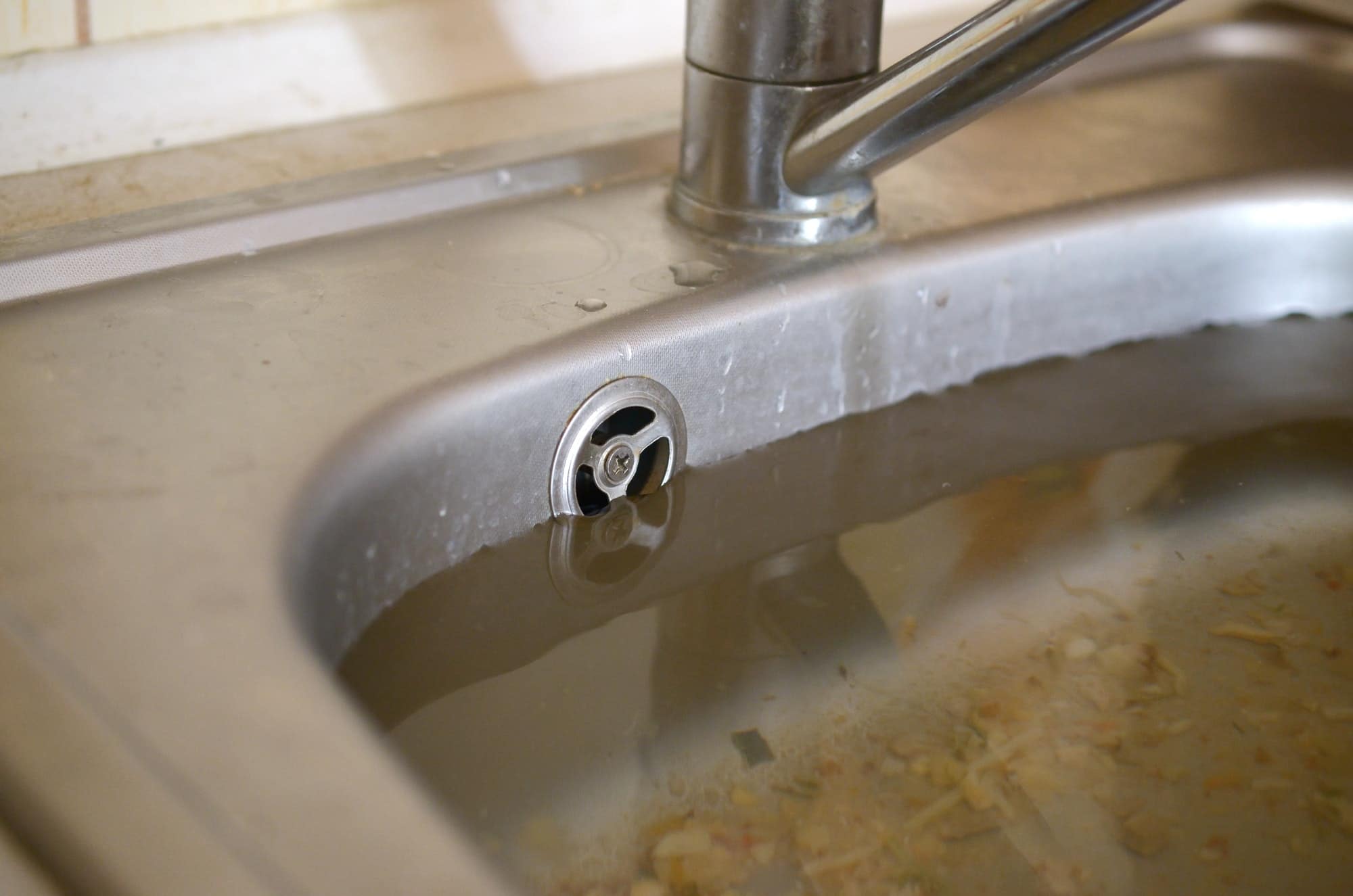 stainless-steel-sink-plug-hole-close-up-full-of-water-and-particles-of-food